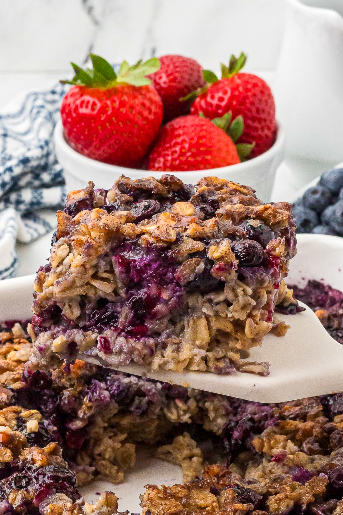 Baked oatmeal with blueberries on a white spatula with fresh strawberries in the background. 