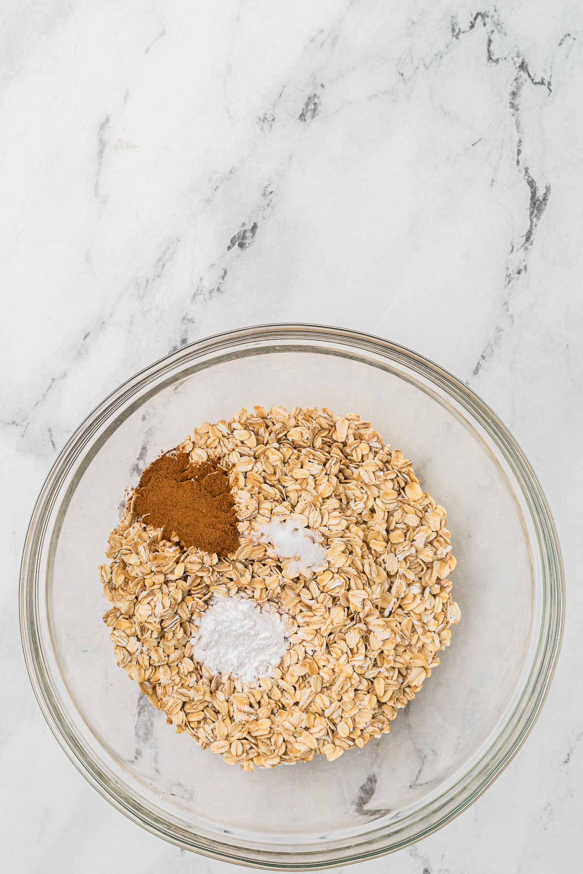 Old-fashioned oatmeal and spices in a clear mixing bowl. 