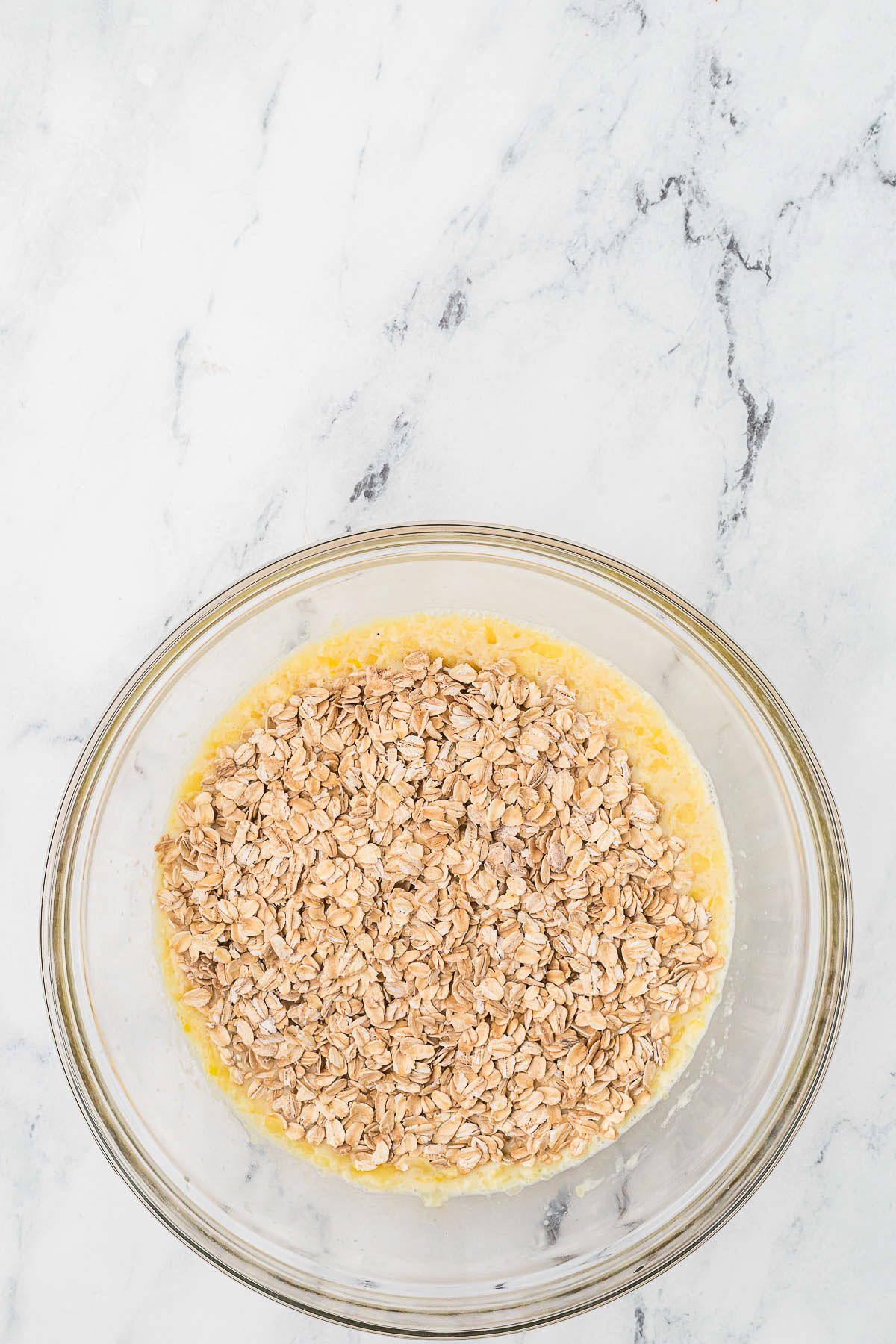 Mixing wet and dry ingredients in a clear mixing bowl for oatmeal bake. 