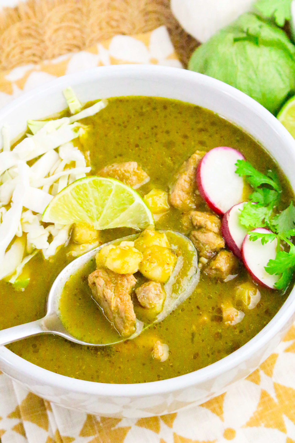 A white serving bowl filled with pork pozole made with green tomatillos. 